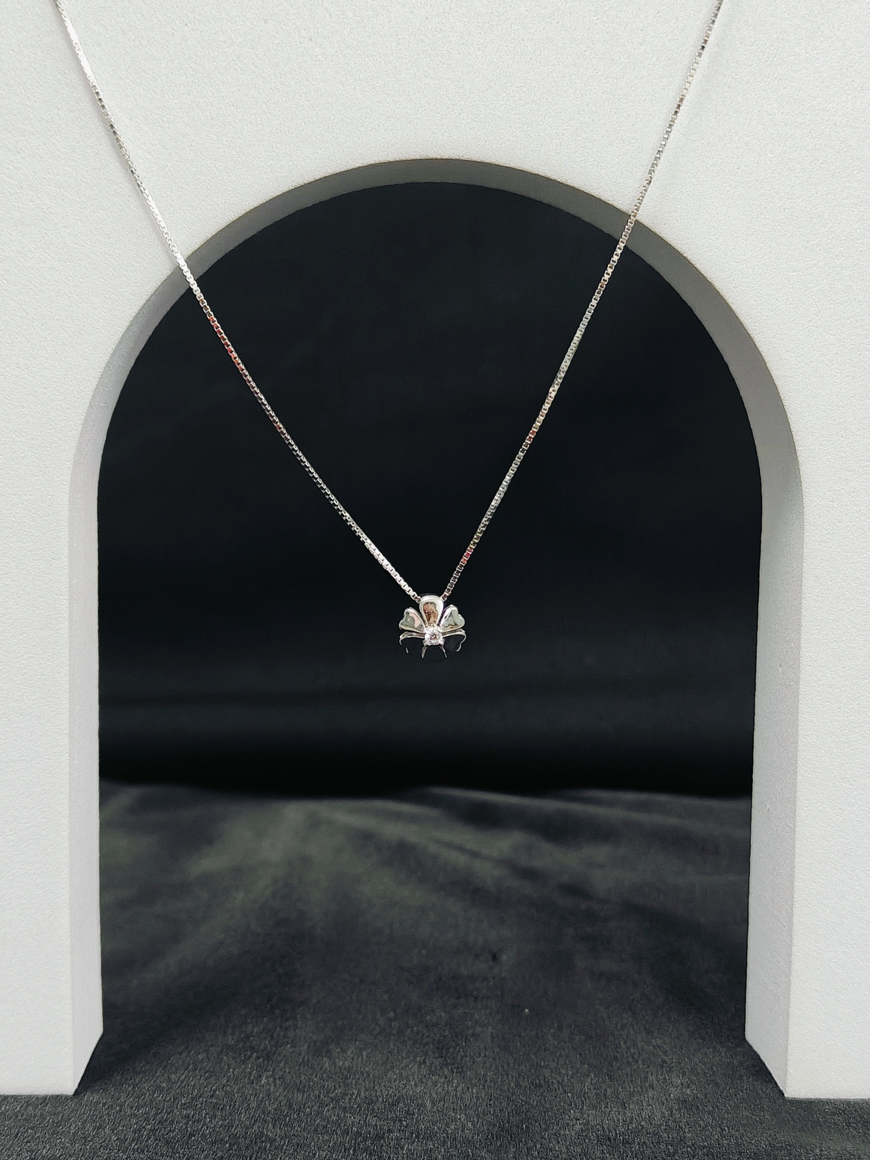 Necklace with a pendant hanging in front of a black archway on a gray surface.